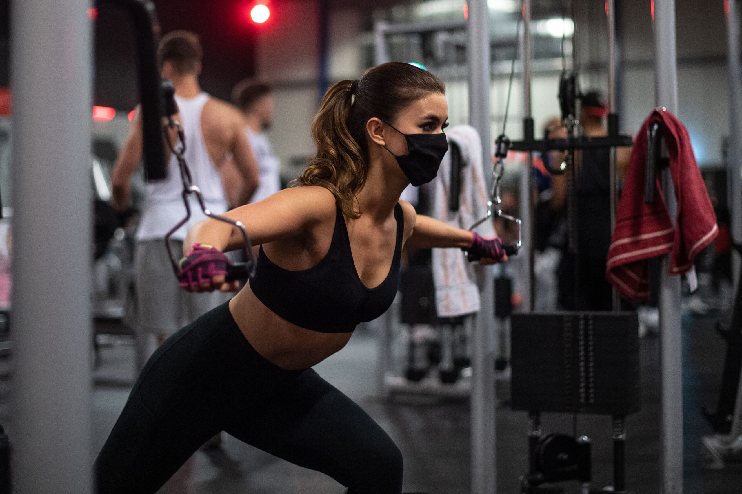 Eine Frau mit Mundschutz trainiert in einem Fitnessstudio der Kette McFit an einem Seilzug.