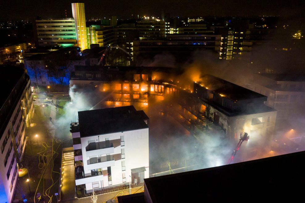 Flammen schlagen aus vielen Fenstern eines Wohnblocks, Feuerwehren versuchen das Feuer zu löschen