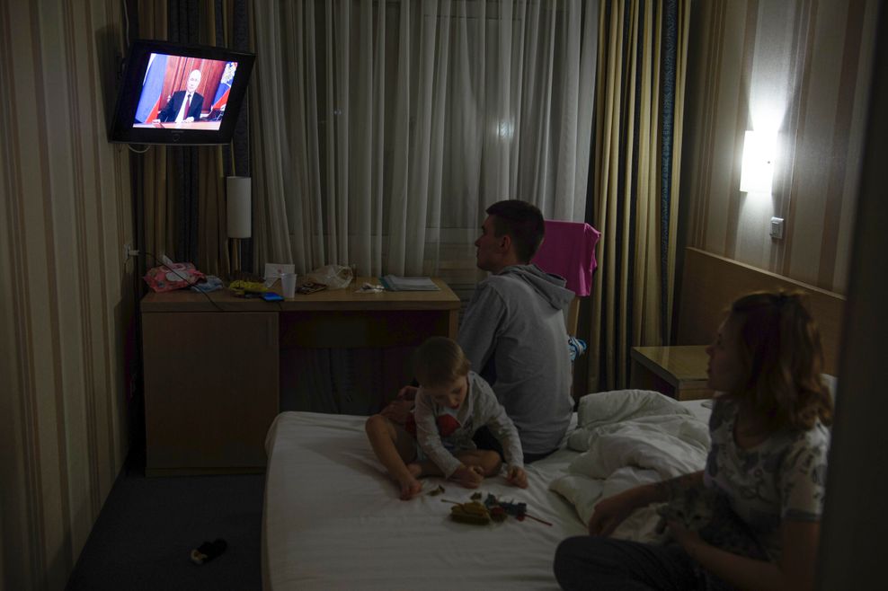 Menschen sitzen in einem Hotelzimmer auf dem Bett und schauen Fernsehen