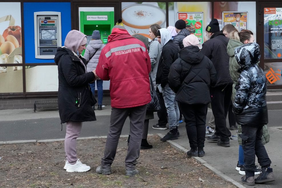 Menschen stehen Schlange, um noch ihr Geld an einem Geldautomaten abzuheben. 