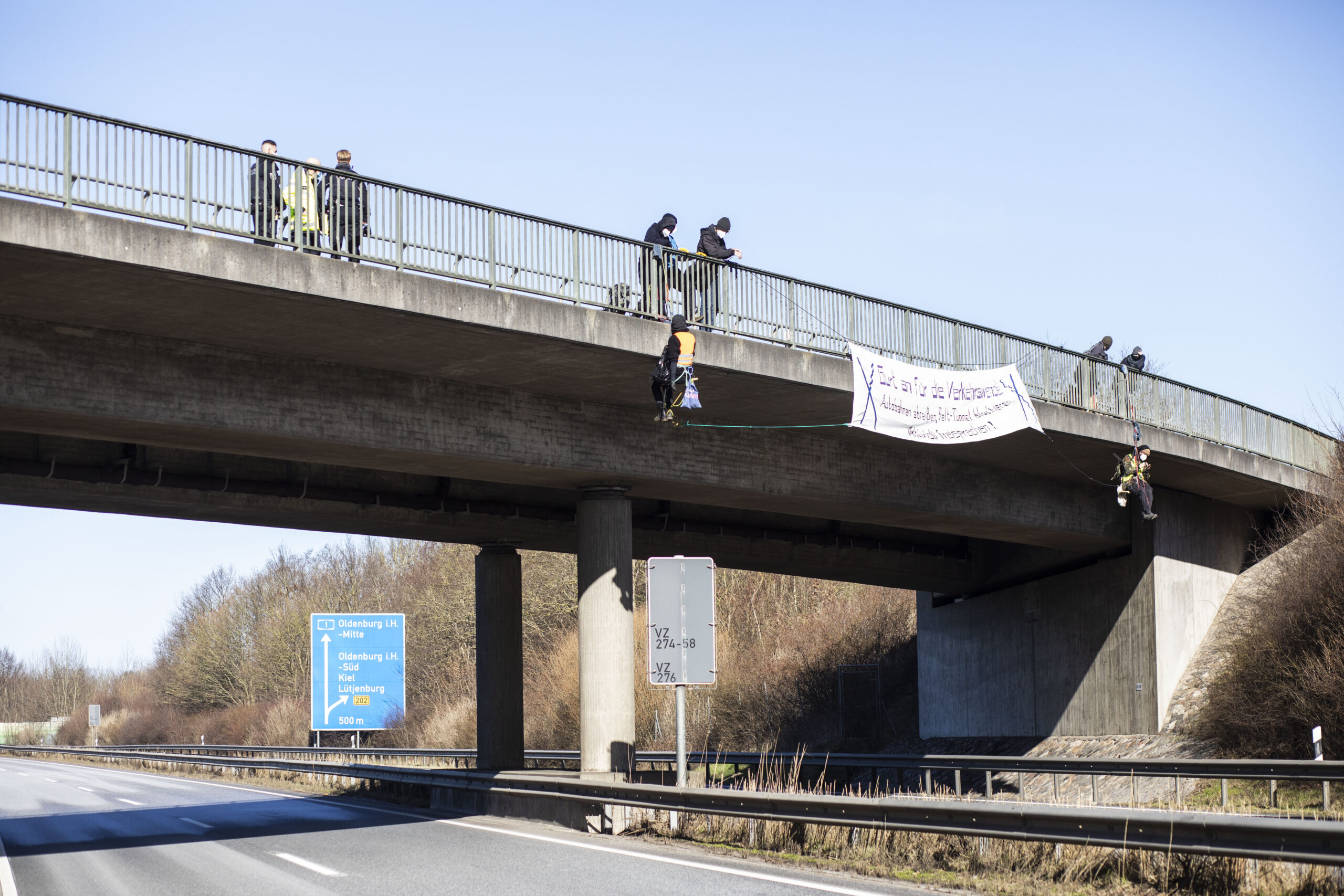 Zwei Personen seilen sich von einer Autobahnbrücke ab, auf der ein Plakat angebracht ist ("Gurt an für die Verkehrswende")