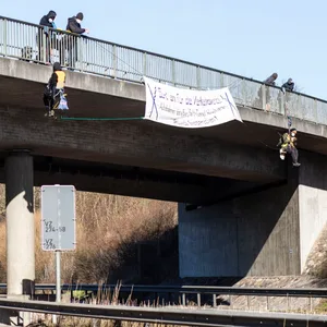 Zwei Personen seilen sich von einer Autobahnbrücke ab, auf der ein Plakat angebracht ist ("Gurt an für die Verkehrswende")