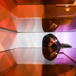 Eine Frau beugt sich nach unten, um besser in ein rotes Kunstwerk aus Plexiglas sehen zu können.