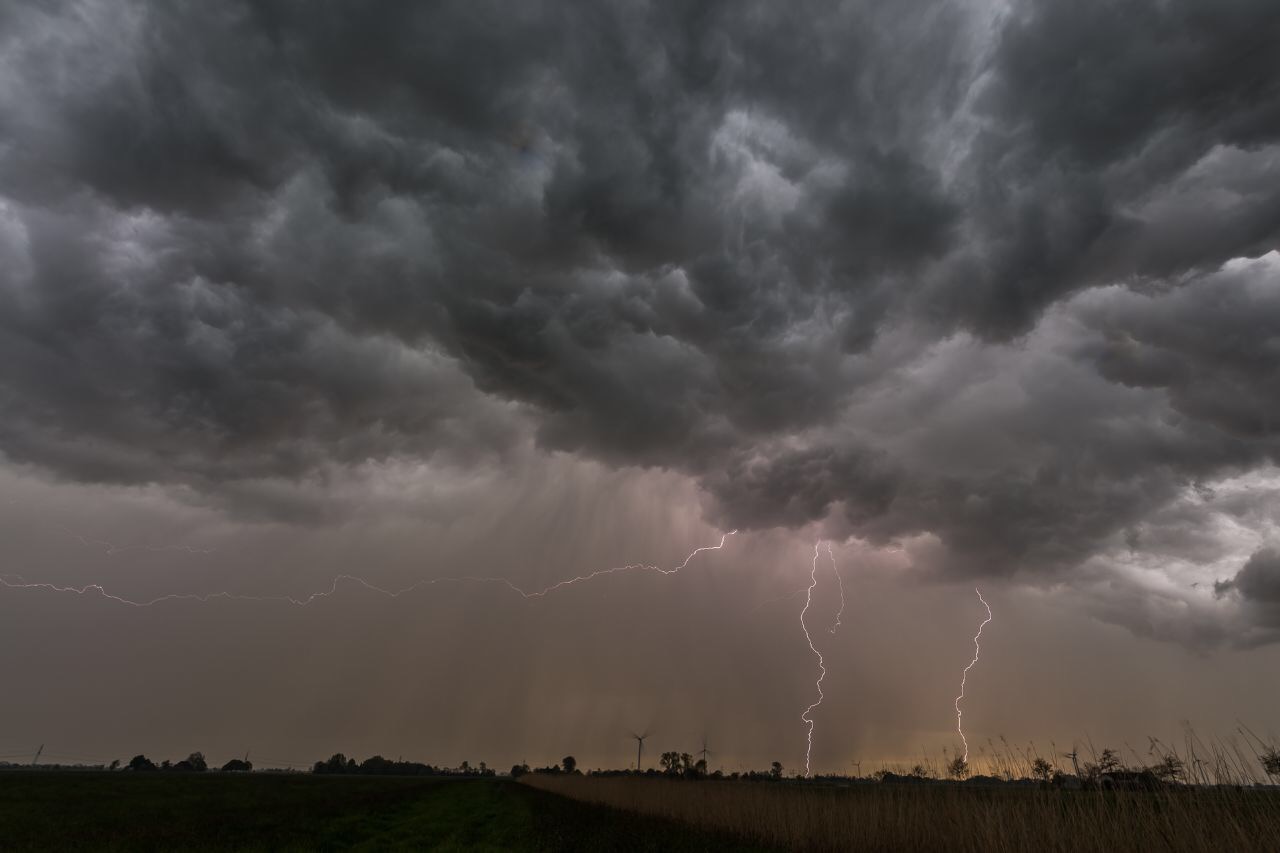 Gewitterwolken mit mehreren Blitzen hängen über einer Wiese.