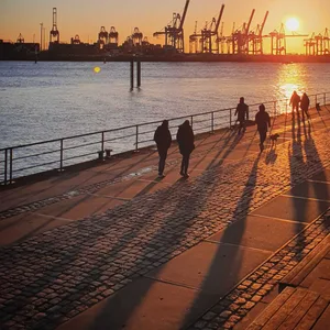 Menschen gehen bei Sonnenuntergang an der Hamburger Hafenpromenade spazieren.