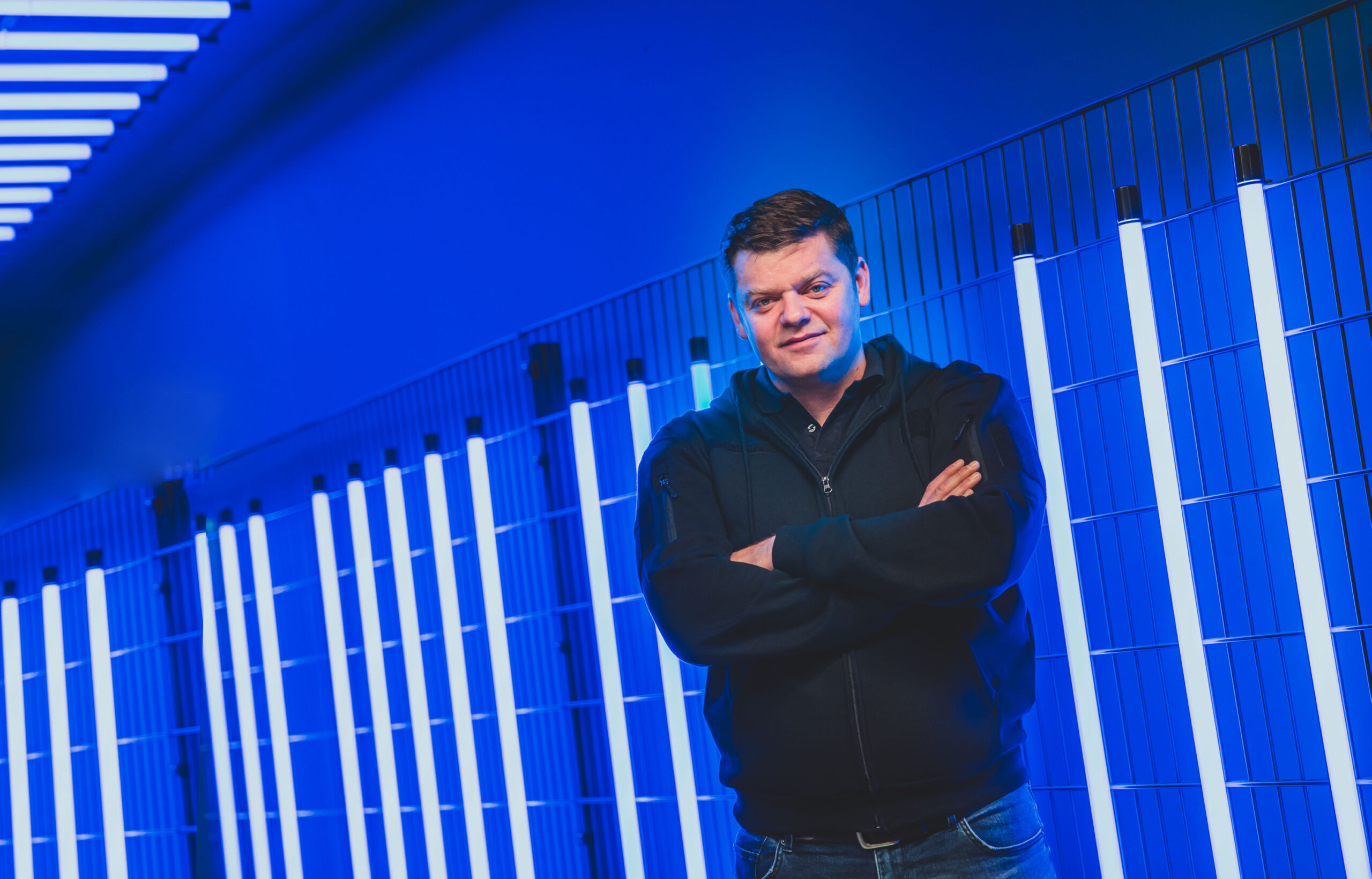 Tomislav Karajica steht vor einer blau angestrahlten Wand mit Neonröhren.