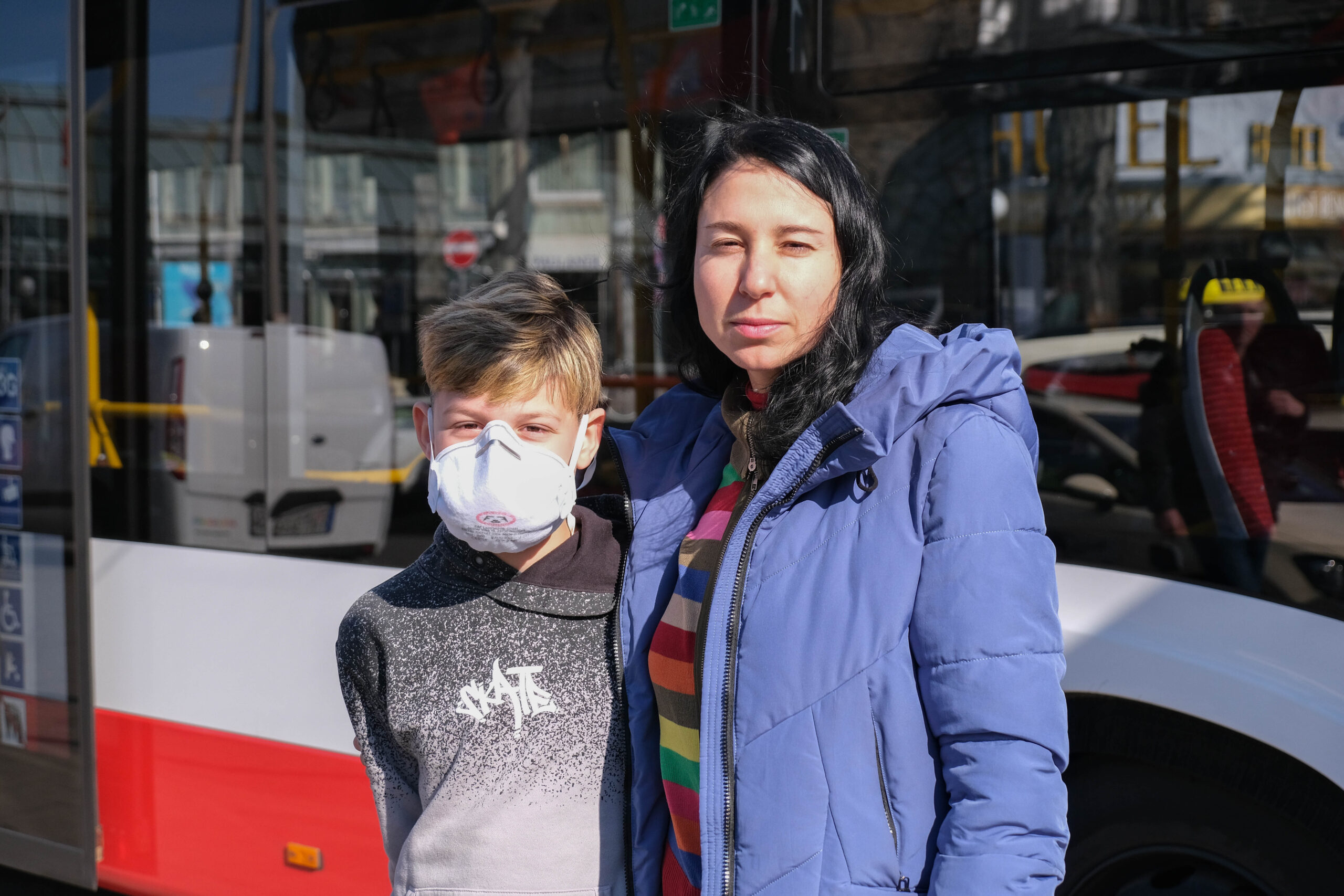 Mutter und Sohn stehen vor einem Bus der HOCHBAHN in der Sonne.