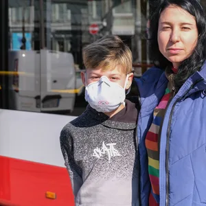 Mutter und Sohn stehen vor einem Bus der HOCHBAHN in der Sonne.