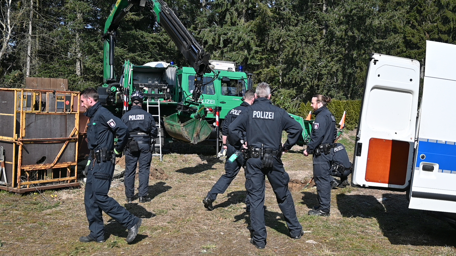 Polizisten stehen vor einem Bagger