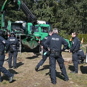 Polizisten stehen vor einem Bagger