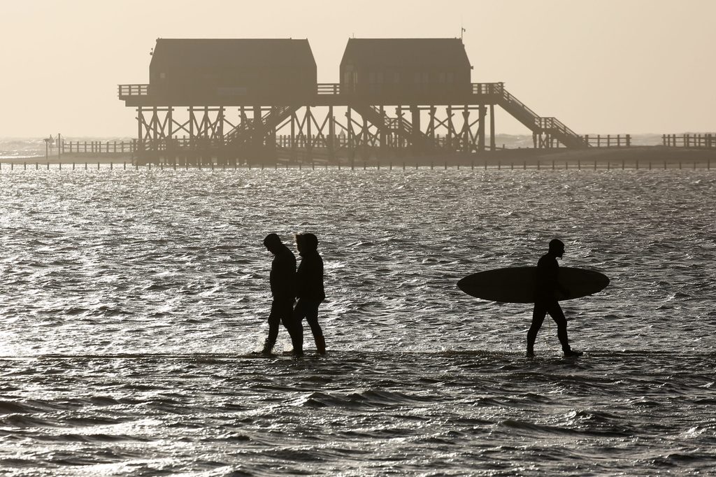 Surfer und Spaziergänger am Strand St. Peter-Ording mit Blick auf Stelzenbauten.