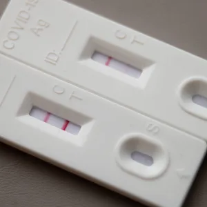 Symbolbild: Ein positiver Corona-Schnelltest (l) liegt auf einem Tisch neben einem Corona-Schnelltest, der schwach eine positive Linie hat.