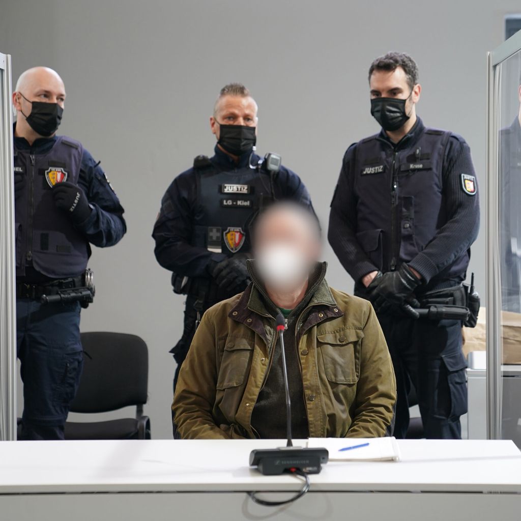Der Angeklagte Hartmut F. im Landgericht Kiel, bewacht von drei Justizbeamten.