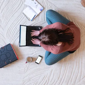 Eine Frau sitzt im Homeoffice auf dem Teppich und arbeitet am Laptop.