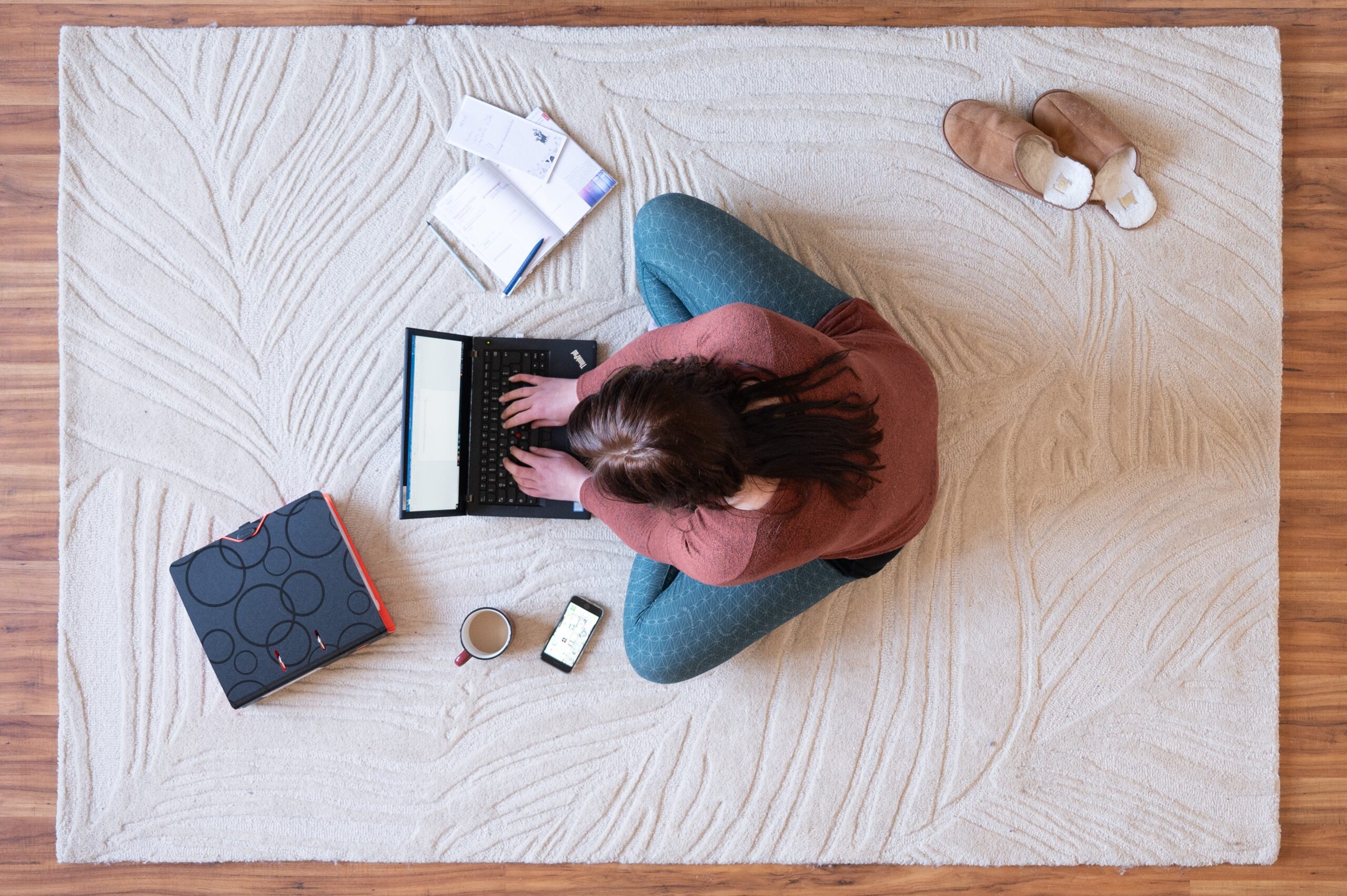Eine Frau sitzt auf dem Teppich im Homeoffice und arbeitet an einem Laptop.