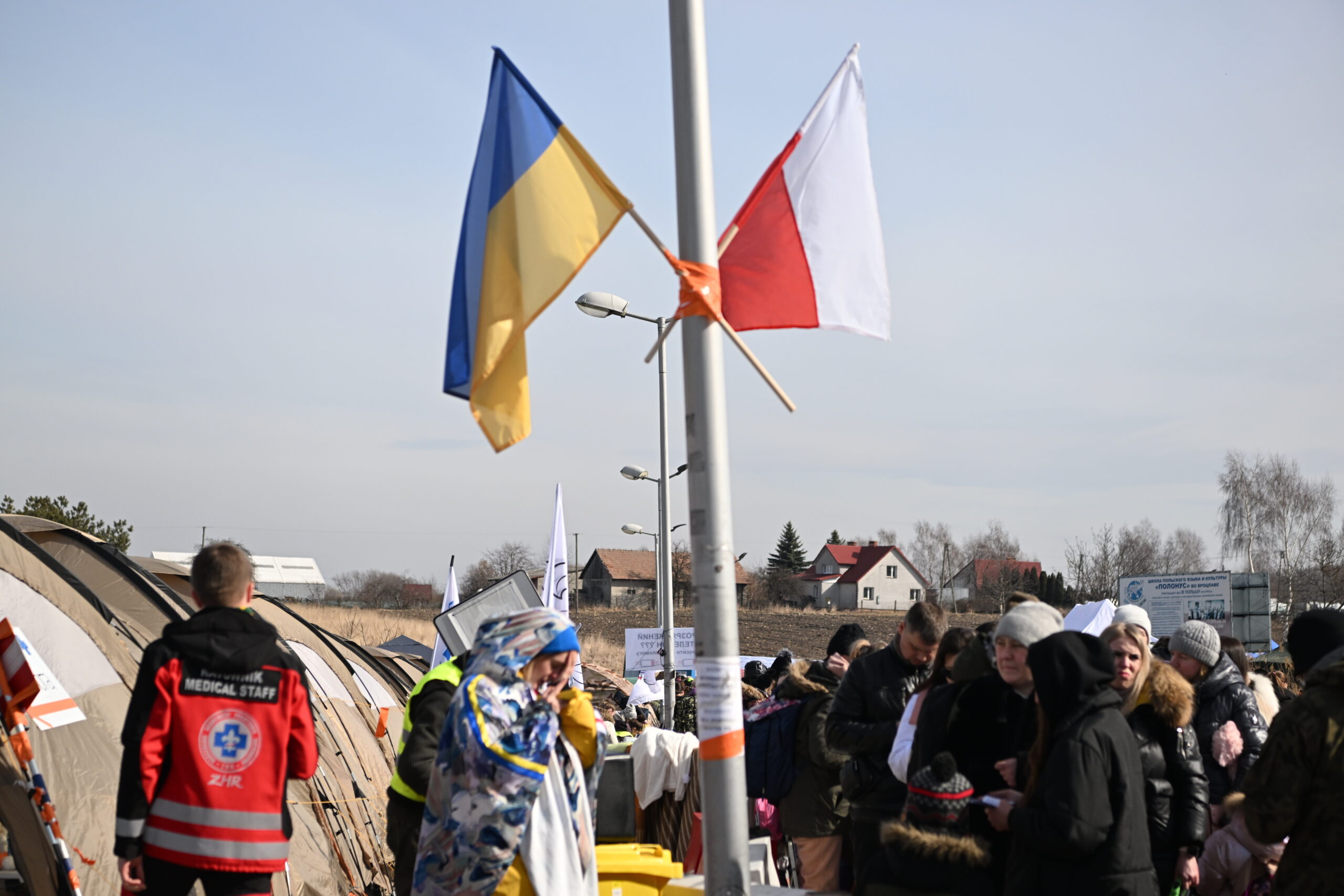 Die polnische und ukrainische Fahne hängen an einem Laternenmast nahe der Grenze, während sich dort Geflüchtete versammeln.