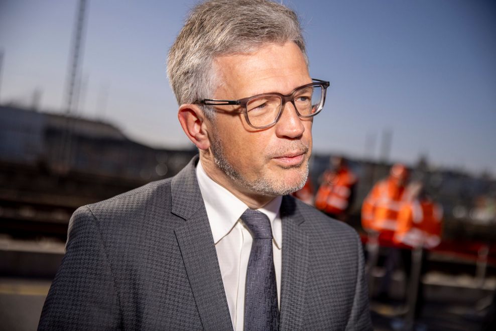 Ein Mann im Anzug und mit Brille spricht bei Interviews nach der Abfaht eines Zuges mit Hilfsgütern für Ukraine