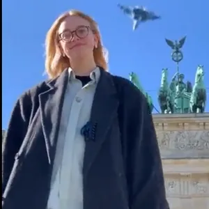 Eine junge Frau vor dem Brandenburger Tor – im Hintergrund ein Jet.