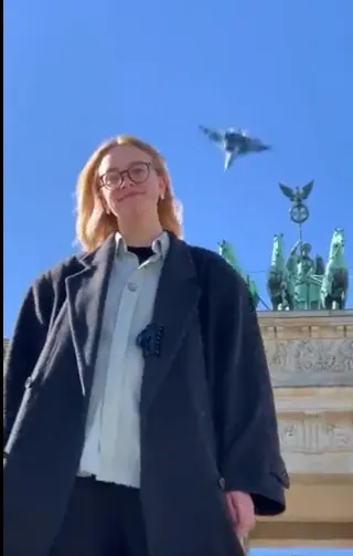 Eine junge Frau vor dem Brandenburger Tor – im Hintergrund ein Jet.