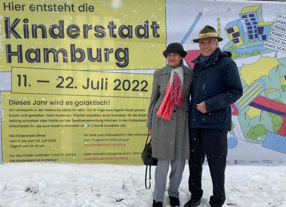 Das Ehepaar Otto steht vor einer Plakatwand im Schnee.
