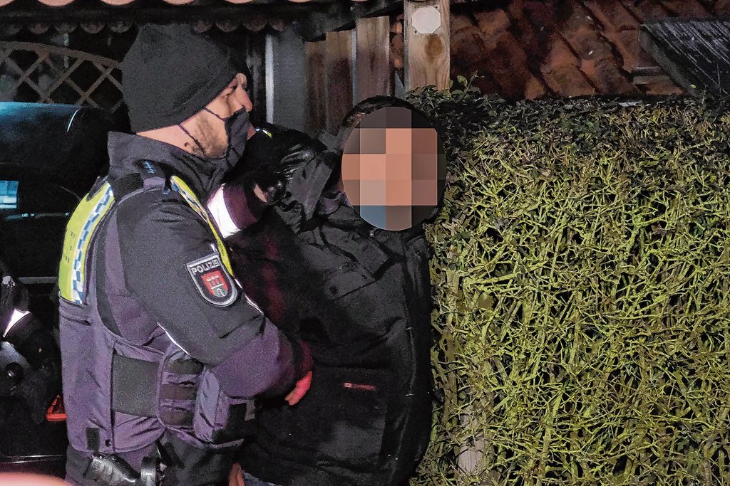 Ein Polizeibeamter nimmt den unkenntlich gemachten Angeklagten fest.