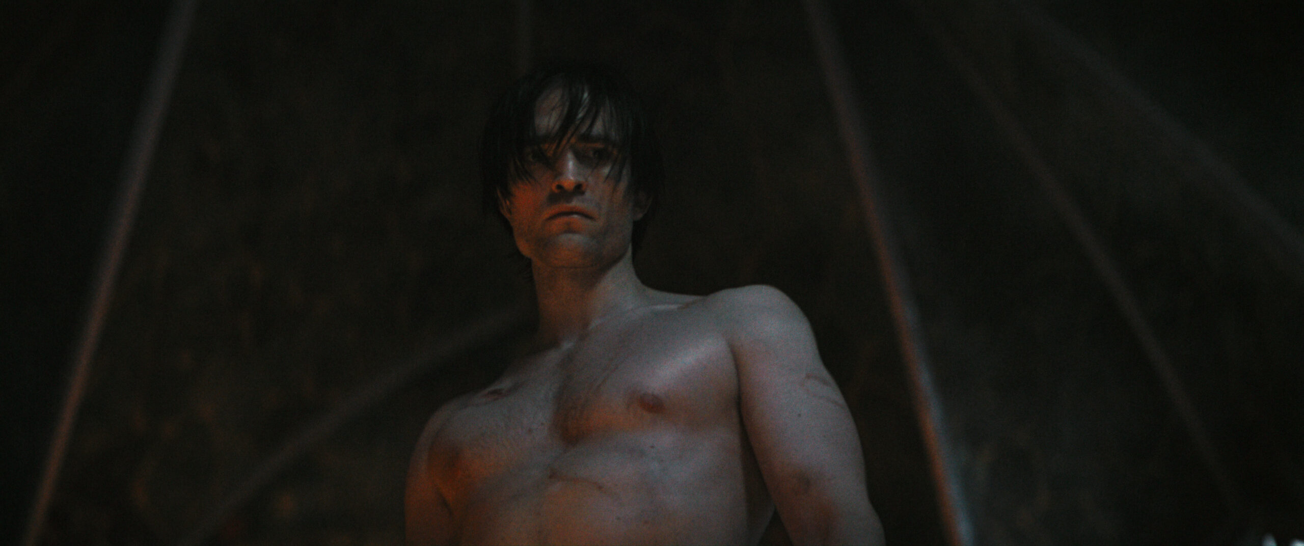Das sehr dunkle Bild zeigt Robert Pattinson mit nacktem Oberkörper