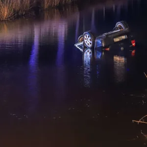 An einer Landstraße stehen Polizei- und Rettungswagen, daneben im Wassergraben liegt kopfüber ein Auto