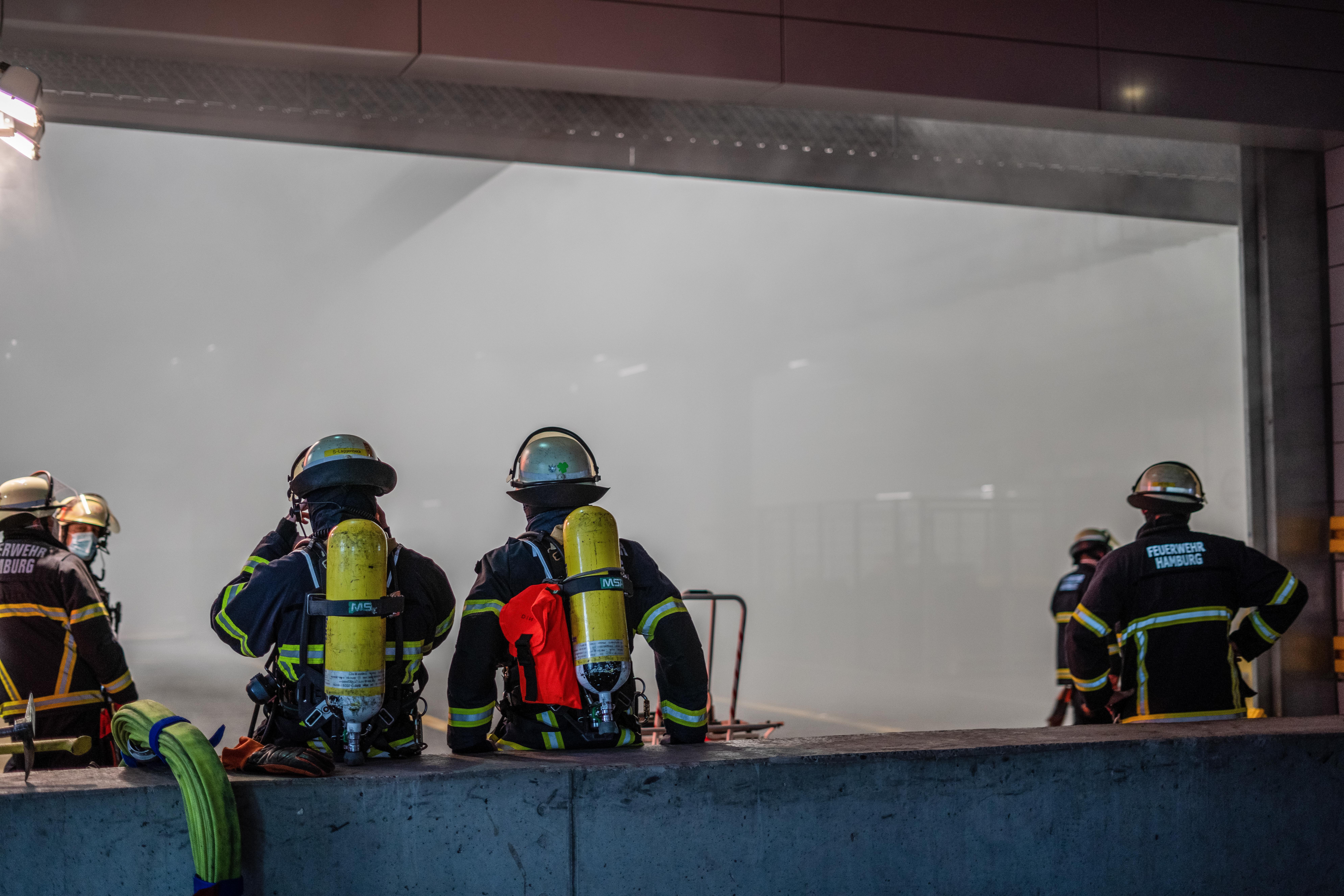 Feuerwehrleute stehen am Eingangsbereich einer Tiefgarage, wo sich starker Rauch gebildet hat