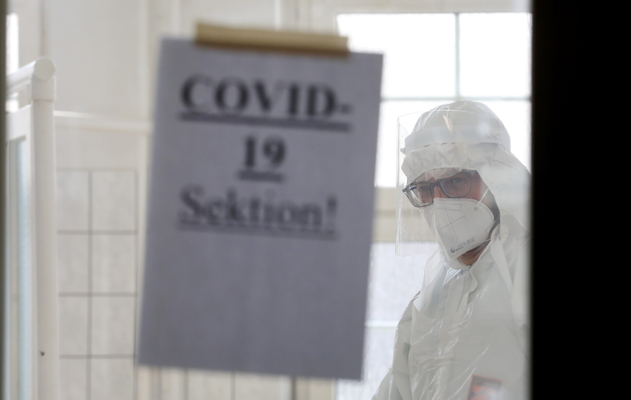 Rechtsmediziner im Leichenhaus blickt auf ein Schild mit der Aufschrift „COVID-19 Sektion!“
