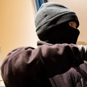 Ein als Einbrecher verkleideter Mann hebelt ein Fenster auf. (Symbolbild)