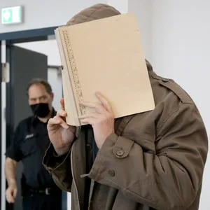 Der 56-jährige Angeklagte, der eine Frau geschlagen und angezündet haben soll, hält sich beim Prozessauftakt Mitte März einen Ordner vors Gesicht.