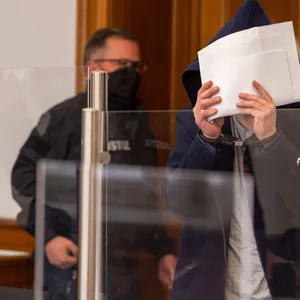 Der Angeklagte wird in den Saal vom Landgericht geführt und verdeckt sein Gesicht. Dem 38-Jährigen wird vorgeworfen, im Oktober 2021 in Lüneburg seine im 7. Monat schwangere Lebensgefährtin durch Messerstiche getötet zu haben.