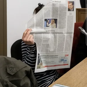 Die Angeklagte verbirgt im Gerichtssaal im Oberlandesgericht ihr Gesicht hinter einer Zeitung neben ihrem Anwalt.