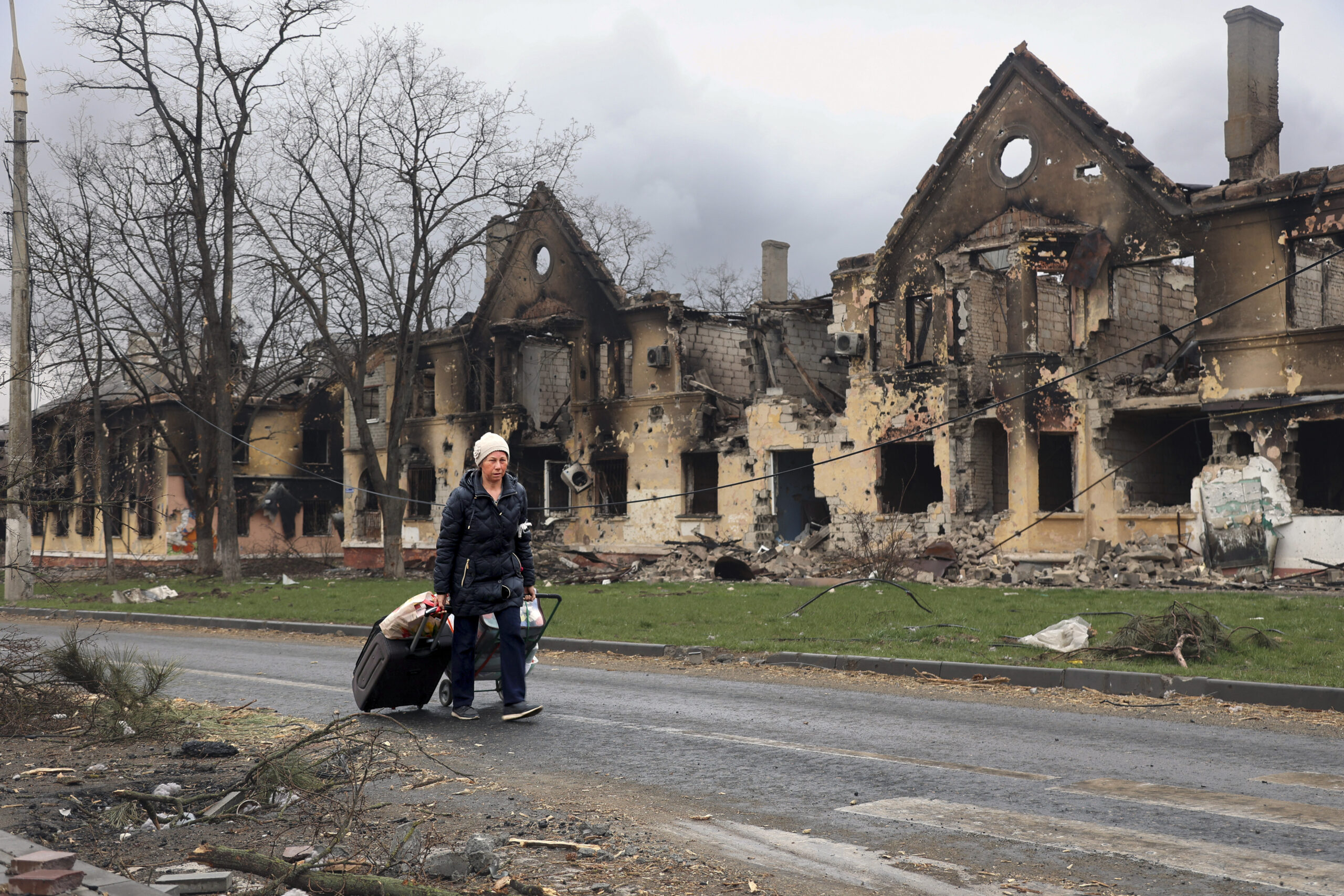 Eine Frau zieht ihre Taschen an Häusern vorbei, die während der Kämpfe in Mariupol beschädigt wurden.