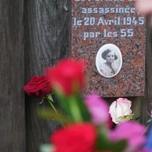 Eine Frau steckt Rosen an den Gedenktafeln der getöteten Kinder im Rosengarten der Gedenkstätte Bullenhuser Damm.