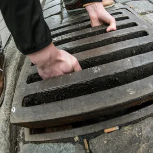 Eine Person hebt einen Gullideckel heraus