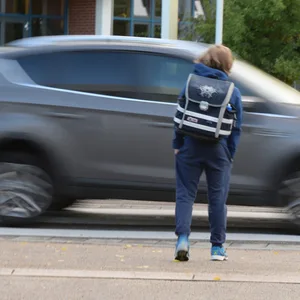 Ein Junge steht an einem Zebrastreifen, über den gerade ein Auto fährt
