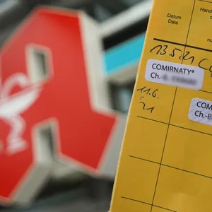 Ein Impfpass wird vor einer Apotheke in die Kamera gehalten (Symbolfoto)