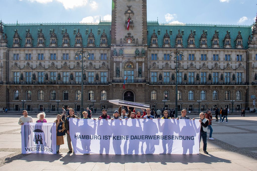 Anhänger der Initiative „Hamburg Werbefrei“ halten vor dem Hamburger Rathaus einen Banner mit der Aufschrift „Hamburg ist keine Dauerwerbesendung“ in den Händen.
