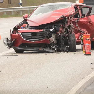 Ein rotes Auto mit zerstörter Front steht auf der Straße, daneben Polizisten