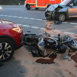 Ein Motorrad liegt auf der Seite, ein silbernes Auto ist an der Vorderseite zerstört, dahinter ein Krankenwagen