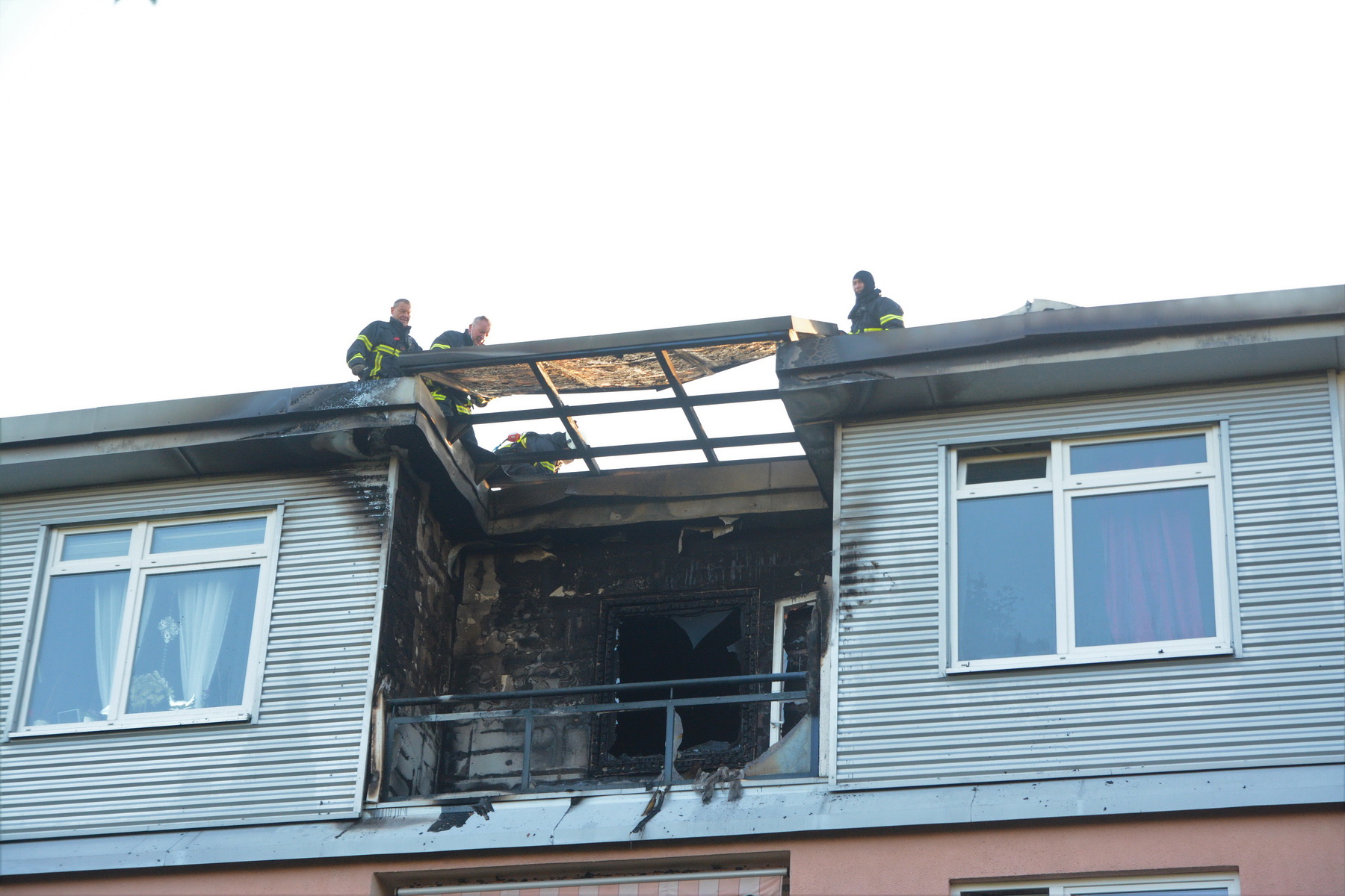 Feuerwehrkräfte nehmen Dachpfannen ab, um nach Glutnestern zu schauen.