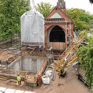 Ein Telekran hebt die 58 Tonnen schwere und 12 Meter hohe Kirchenwand an den neuen Standort hinter der Kirche.