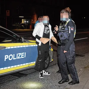 Man sieht den Angeklagten vor einem Polizeiauto stehen.