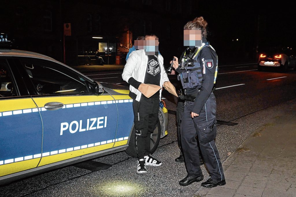 Man sieht den Angeklagten vor einem Polizeiauto stehen.