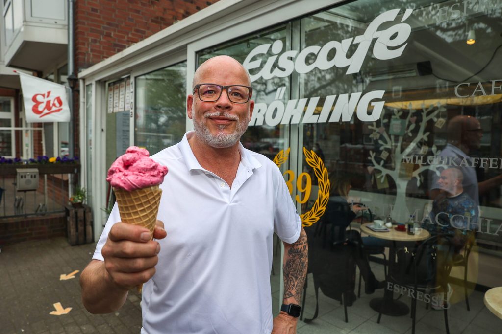 Sven Hobe steht vor seinem Eiscafé Röhling und hält eine Waffel Erdbeereis in der Hand.