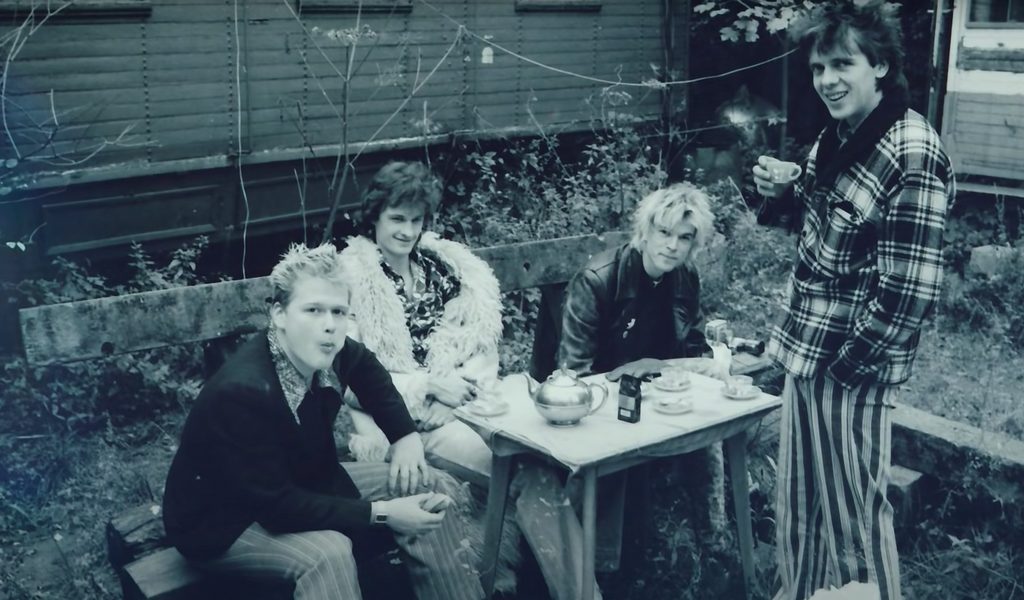 Schwarzweiß-Foto aus dem Video. Die Toten Hosen sitzen draußen im Grünen an einem Tisch und trinken Tee
