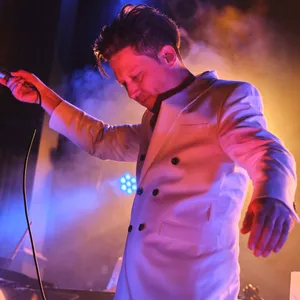 Konstantin Gropper im weißen Anzug auf der Bühne, tanzend mit Mikrofon in der Hand