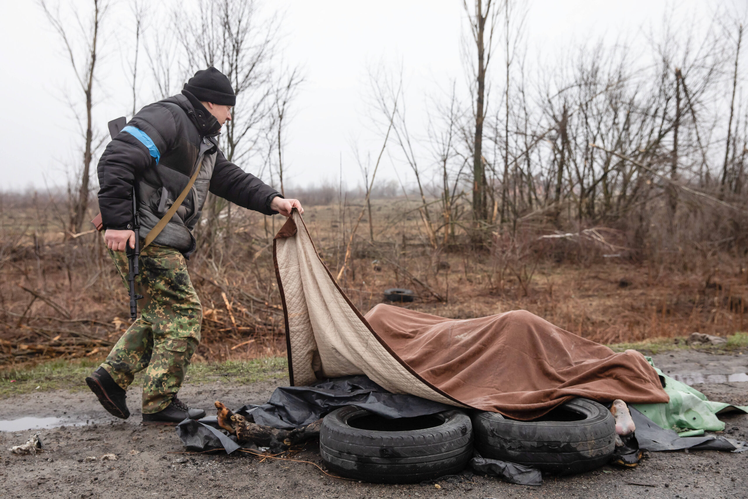Ein ukrainischer Soldat breitet eine Decke über de Leichen mehrerer verbrannter Frauen in Butscha.