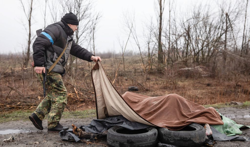Ein ukrainischer Soldat breitet eine Decke über de Leichen mehrerer verbrannter Frauen in Butscha.